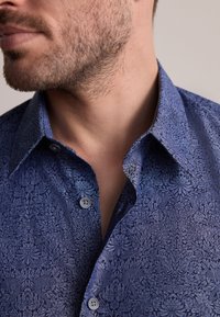 Tumesinine nööbitav särk keerukate lillemustritega, millel on terav krae ja kaks nööpi nööbituval.