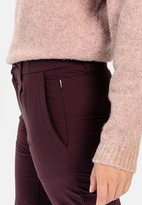Bordeauxfarbene Hosen mit schlanker Passform, ausgestattet mit seitlichen Taschen und dezenten Nähten, kombiniert mit einem hellrosa, flauschigen Pullover.