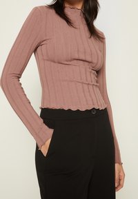 Long-sleeve, ribbed top in mauve with a scalloped collar and hem. Paired with black trousers featuring a button and pockets.