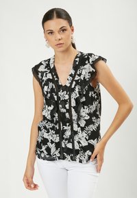 Schwarze Bluse mit floralen Mustern in Weiß, mit Rüschensleeves und tiefem V-Ausschnitt; ergänzt durch zarte schwarze Besatzdetails.