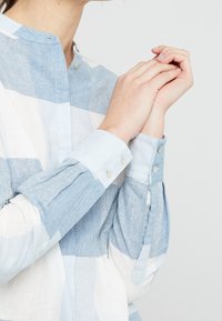 Ljusblå och vitrandig skjorta med mandarin-krage, knappdetaljer och långärmar med knäppta manschetter.