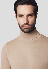 Beżowy sweter z golfem z dzianiny w prążki, o dopasowanym kroju i wysokim kołnierzu. Miękka tekstura z bezszwami wykończeniem.