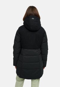 Mustal puffer-takk, millel on kapuuts, funktsionaalne pehmest materjalist lapp, ruuduline disain ja logode plaastriga tagaküljel. Pikkus ulatub keskmise reieni.