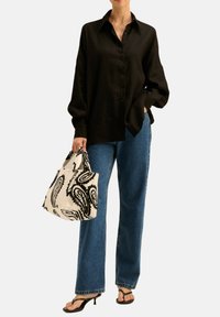 Czarna koszula z guzikami, luźny krój; jasnoniebieskie jeansy z wysokim stanem i prostą nogawką; wzorzysty worek w białym i czarnym kolorze; czarne klapki.