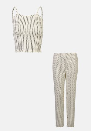 Set format din două piese, cu un top crop fără mâneci și pantaloni asortati. Ambele au o bază cremă cu modele mici de puncte negre.
