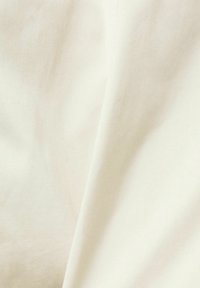 Tissu ivoire doux, légèrement froissé, avec des variations subtiles de lumière et d'ombre, montrant la texture et les plis.