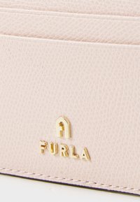 Svijetloružičasti teksturirani kožni novčanik za kartice s utisnutim zlatnim logotipom "FURLA" i detaljima šivanja. Kompaktan dizajn s višestrukim utorima za kartice.