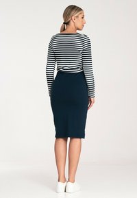 Długi rękaw w paski w kolorze granatowym i białym, w zestawieniu z jednolitą granatową spódnicą do kolan. Materiał wydaje się miękki i elastyczny, dopełniony białymi butami casualowymi.