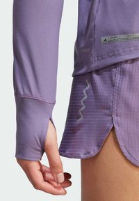 Paarse sporttop met lange mouwen en duimgaten, gecombineerd met een stoffen paarse rok. Beide kledingstukken hebben een ademend ontwerp.