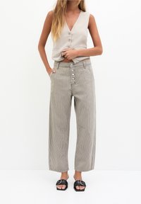 Light gray sleeveless top with button closure, paired with wide-leg striped trousers featuring front pockets and a five-button fly. Black slide sandals.