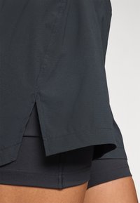 Dark gray athletic shirt with side slits, made from lightweight fabric, layered over matching shorts with flat seams.