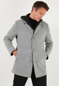 Šedý kabát z vlněné směsi s kapucí, vybavený detailním zapínáním na knoflíky, dvěma bočními kapsami a elegantním designem. Viditelná vnitřní vrstva.