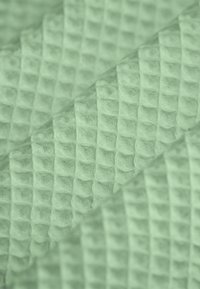 Grüner, strukturierter Stoff mit einem erhobenen Waffelmuster, das ein weiches, kuscheliges Aussehen und diagonale Falten zeigt.