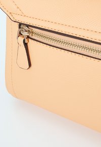 Peach-colored textured faux leather bag corner, featuring a metallic zipper with a pull tab and brown stitching accents.