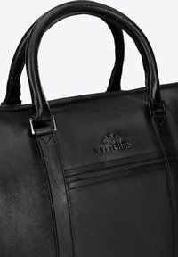 Bolso de cuero negro con doble asa, logotipo embosado y detalles de costura horizontal. Textura suave con acentos de hardware plateado brillante.