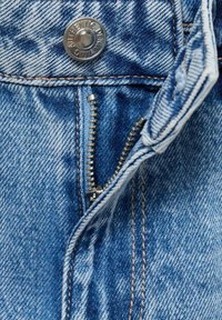Modra jeansa tkanina ima srebrn kovinski gumb z oznako "AVTENTIČEN JEANS" in viden zadrgo z drobnimi zobmi na sprednjem odtvoru.