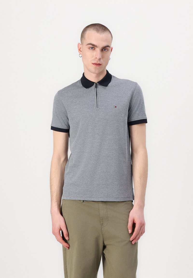Sivá polo tričko s námorníckym golierom a krátkymi rukávmi. Obsahuje zips na prednej strane a malé logo na hrudi. Vyrobené z mäkkej zmesi bavlny.