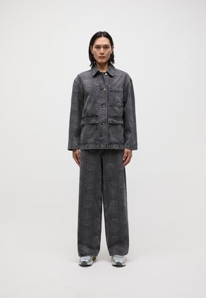 Giacca di jeans grigia con una tasca e design a motivi, abbinata a pantaloni larghi coordinati. Il modello indossa sneakers argentate.