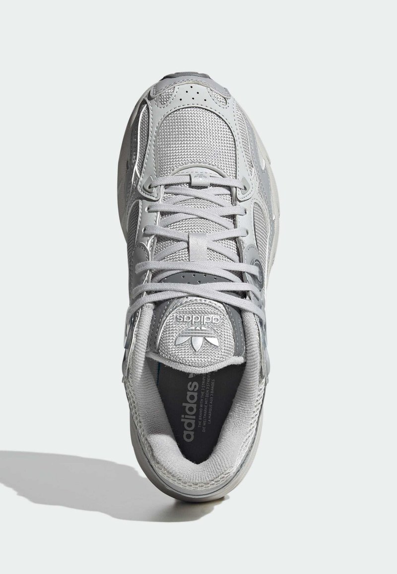 Zapatilla deportiva gris con parte superior de malla, lengüeta acolchada y cordones. Presenta un logo sutil y una suela acolchada para mayor comodidad.