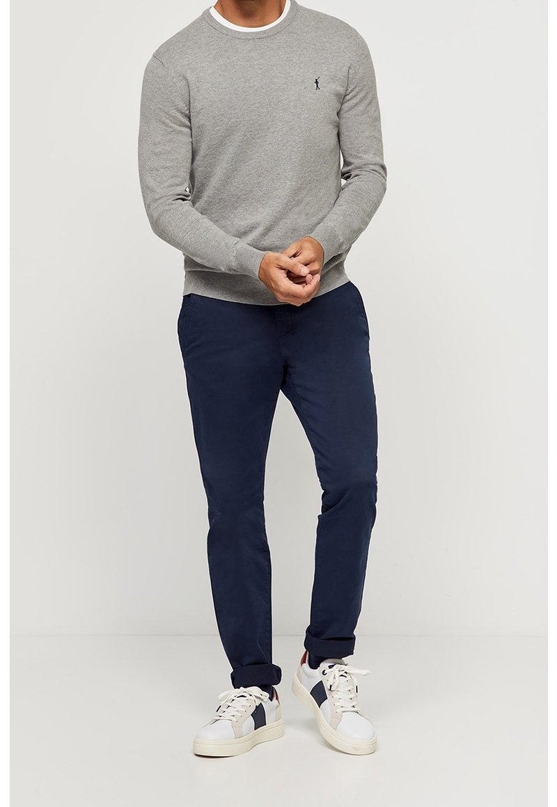 Pull gris à col rond avec poignets côtelés, pantalon bleu marine et baskets blanches avec des accents bleu marine et rouge. Tenue simple et décontractée.