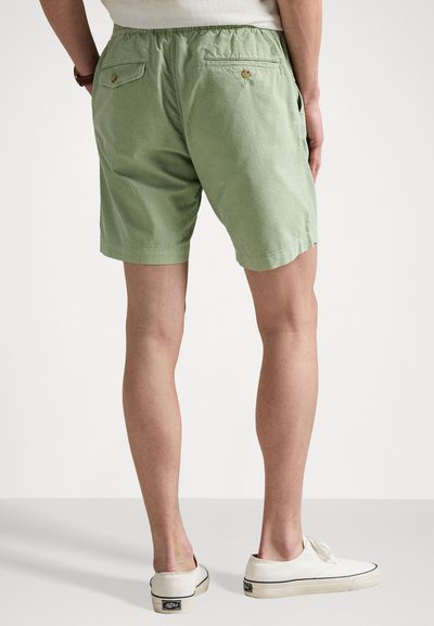 Shorts en coton vert avec une coupe décontractée, une taille élastique et deux poches arrière. Associés à des chaussures blanches et un haut neutre.