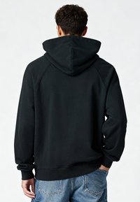 Zwarte capuchontrui met een gladde textuur, raglanmouwen en geribde manchetten. Het zicht toont de achterkant met een ontspannen pasvorm zonder logo's.