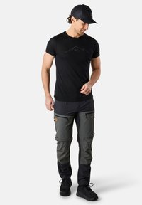 T-shirt noir avec graphique de montagne, et pantalon gris bicolore avec poches zippées et chaussures sombres. Vêtements de sport décontractés pour une utilisation en extérieur.