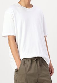 Vit bomull T-shirt med rund halsringning och korta ärmar, bärs tillsammans med olivgröna cargoshorts med sidofickor och elastisk midja.