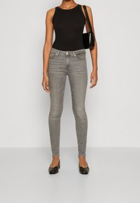 Vaqueros ajustados grises de cintura alta, combinados con una blusa sin mangas negra y zapatos de tacón bloque negro. Se lleva un pequeño bolso negro de hombro.