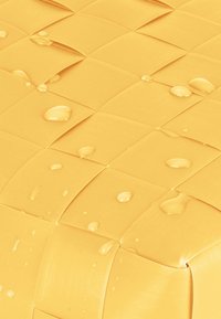 Gewebte gelbe Oberfläche mit einem karierten Muster, auf der Wassertropfen auf einem strukturierten Material zu sehen sind. Glatte und glänzende Oberfläche.