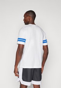 Tricou alb din bumbac cu accente albastre în dungi pe mâneci. Tricoul are un design clasic cu guler rotund și este completat cu shorts negri din plasă.