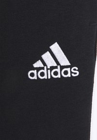 Zwarte stof met een witte geborduurde Adidas-logo en drie diagonale strepen. Glad oppervlak zonder opvallende patronen of hardware.