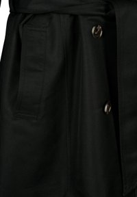 Tissu de trench-coat noir avec une poche rectangulaire et deux gros boutons ronds marron et blanc visibles sur le devant.