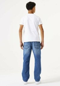 Camiseta blanca de manga corta combinada con jeans de corte holgado en un azul desgastado. Los jeans tienen dos bolsillos traseros y un ligero degradado en el color.