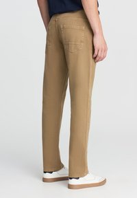 Pantaloni di cotone color cammello con una vestibilità dritta, dotati di due tasche posteriori e indossati con sneakers bianche.