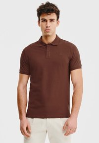 Brązowa koszulka polo wykonana z bawełny, z klasycznym kołnierzykiem, zapięciem na dwa guziki, krótkimi rękawami i minimalnym logo na klatce piersiowej.