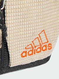 Zaino beige texturizzato con chiusura a zip, dotato di un logo ricamato arancione e fondo in materiale nero maculato.