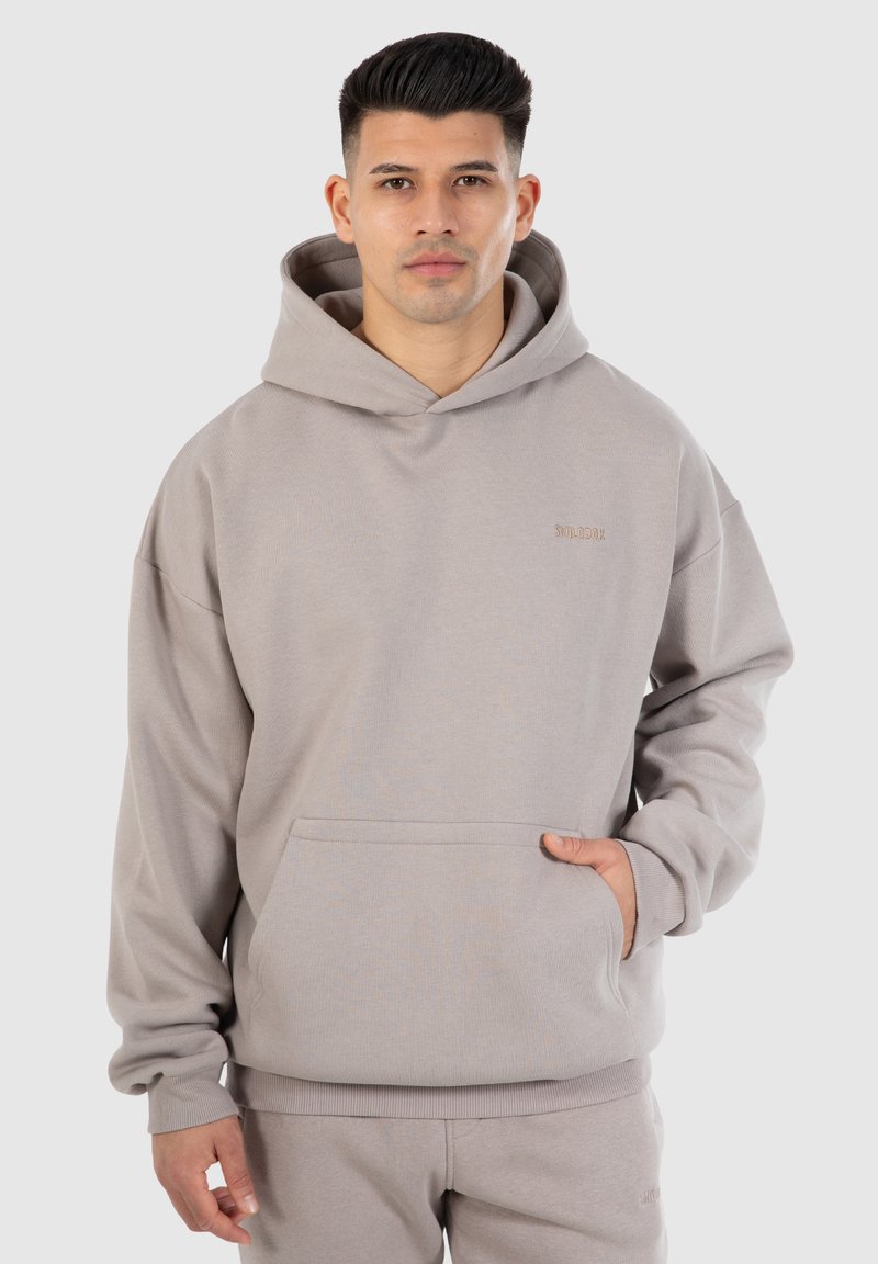 Grauer Kapuzenpullover aus weichem Stoff mit einer Fronttasche. Verfügt über eine lockere Passform und gerippte Bündchen. Dezentes Logo-Detail in passender Farbe.
