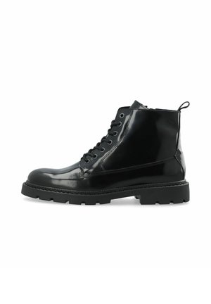 Bottine en cuir noir brillant avec laçage sur le devant, semelle crantée épaisse et languette à l'arrière.
