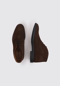 Zapatos de ante marrón con puntera redondeada y tacón bajo. Cuentan con cordones, textura suave y una suela de goma negra a contraste.