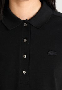 Gros plan d'un polo noir avec quatre boutons et un petit logo crocodile brodé sur la poitrine.