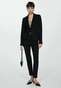 Black tailored blazer and pants set, with a gray top. Accessories include a small handbag and black pointed-toe flats. Smooth texture, structured fit.