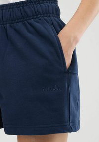 Marineblaue Shorts aus weichem Stoff mit einem elastischen Bund und Seitentaschen. Texturiertes Logo an dem Unterschenkel.
