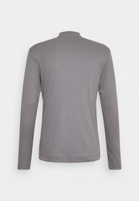 Pull en maille gris à manches longues avec un col rond haut, montré de dos sur un fond clair uni.