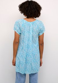 Tunique à motif floral bleu avec des manches courtes et un col rond. Fabriquée en tissu léger, elle présente une coupe ample et un dos plissé.