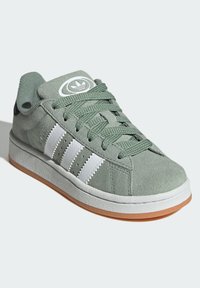 Zelené semišové sneakers s bielymi pruhmi, textúrovaným šnurovacími detailami, gumovou podrážkou a logom na jazyku. Obsahuje polstrovaný golier pre pohodlie.