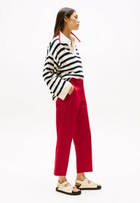 Pull en tricot rayé crème et marine avec un col rouge, associé à un pantalon droit rouge vif et des sandales beiges avec des semelles noires.