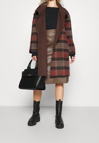 Abrigo de cuadros marrón con una capa interior negra, falda de cuero marrón, bolso negro y botines negros con suelas gruesas.