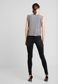 Top gris sin mangas con un corte holgado, combinado con jeans skinny negros y sandalias negras de tacón alto con detalles metálicos en los tobillos.