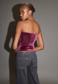 Bordó sametový top bez ramínek v kombinaci s vysokým pasem tmavě šedých džínů s cvočky podél pasu. Hladká textura, přiléhavý střih.
